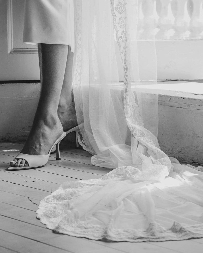Person wearing a white dress with a sheer overlay and high-heeled shoes on a wooden floor.